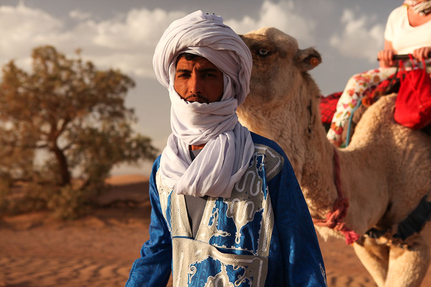Portrait of a guide in a white turban beside his camel